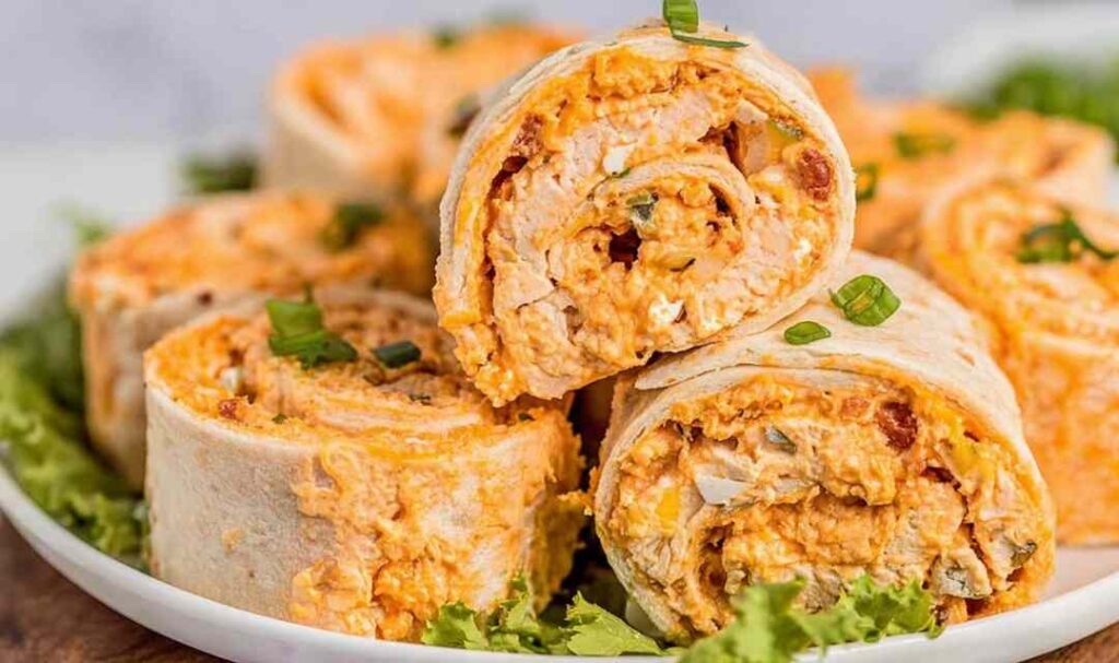 Buffalo Chicken Pinwheels arranged on a white serving platter with celery sticks and blue cheese dipping sauce on the side