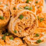 Buffalo Chicken Pinwheels arranged on a white serving platter with celery sticks and blue cheese dipping sauce on the side