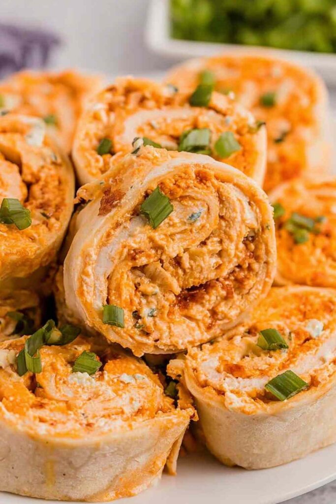 Buffalo Chicken Pinwheels arranged on a white serving platter with celery sticks and blue cheese dipping sauce on the side