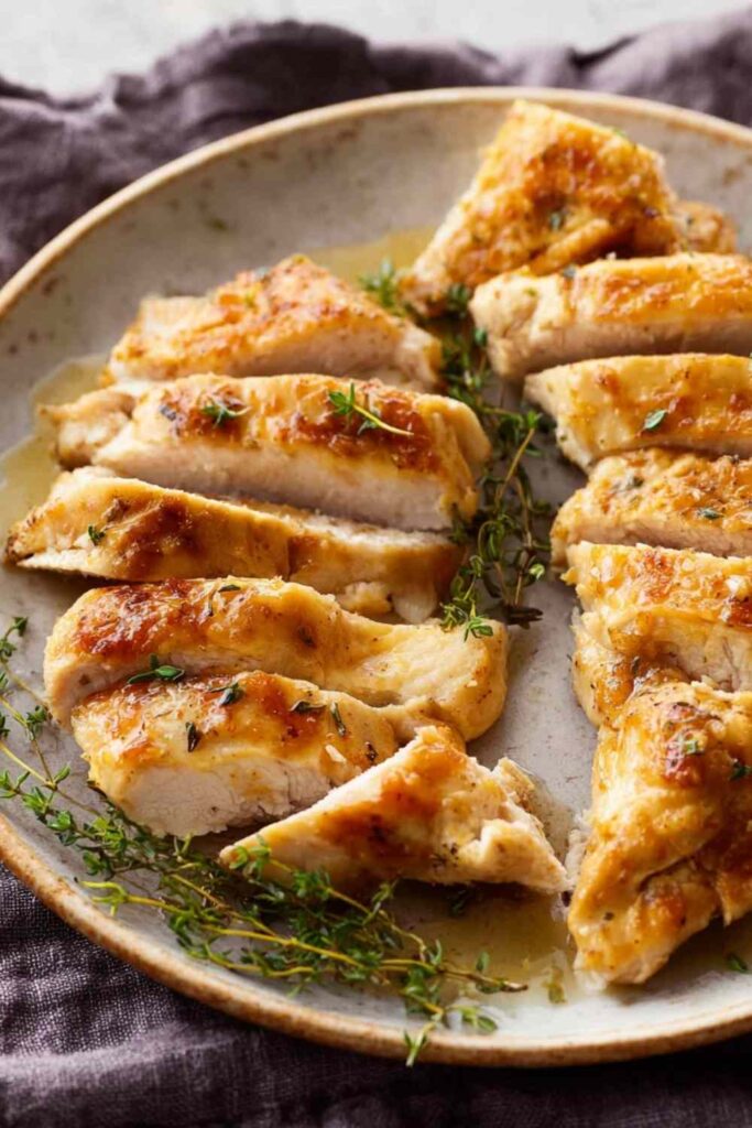 Butter baked chicken in a white baking dish with creamy white gravy bubbling around golden flour-coated chicken breasts fresh from the oven