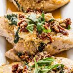 Chicken Bryan Carrabba's copycat with melted goat cheese and sun-dried tomato cream sauce on a white plate with fresh basil