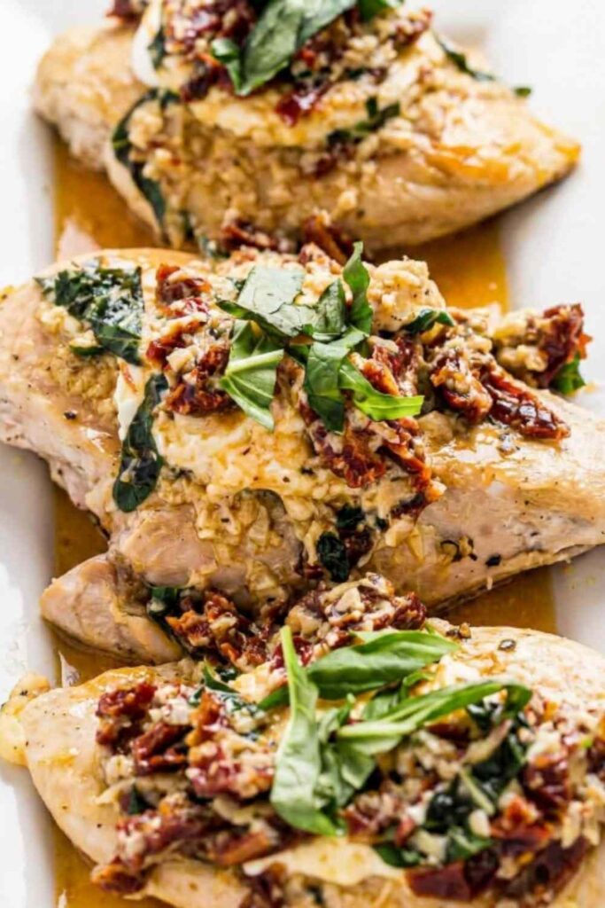 Chicken Bryan Carrabba's copycat with melted goat cheese and sun-dried tomato cream sauce on a white plate with fresh basil