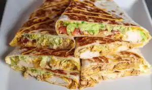 Homemade chicken crunchwrap supreme cut in half diagonally showing crispy tostada shell with layers of shredded chicken, queso blanco, guacamole, and melted Monterey Jack cheese inside a golden flour tortilla