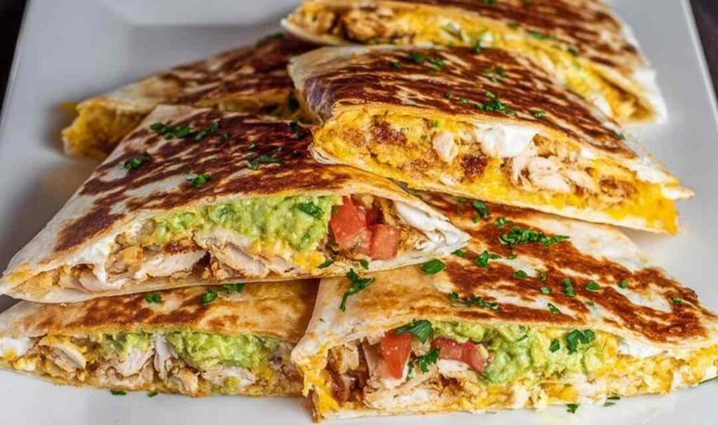 Homemade chicken crunchwrap supreme cut in half diagonally showing crispy tostada shell with layers of shredded chicken, queso blanco, guacamole, and melted Monterey Jack cheese inside a golden flour tortilla