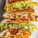 Homemade chicken crunchwrap supreme cut in half diagonally showing crispy tostada shell with layers of shredded chicken, queso blanco, guacamole, and melted Monterey Jack cheese inside a golden flour tortilla