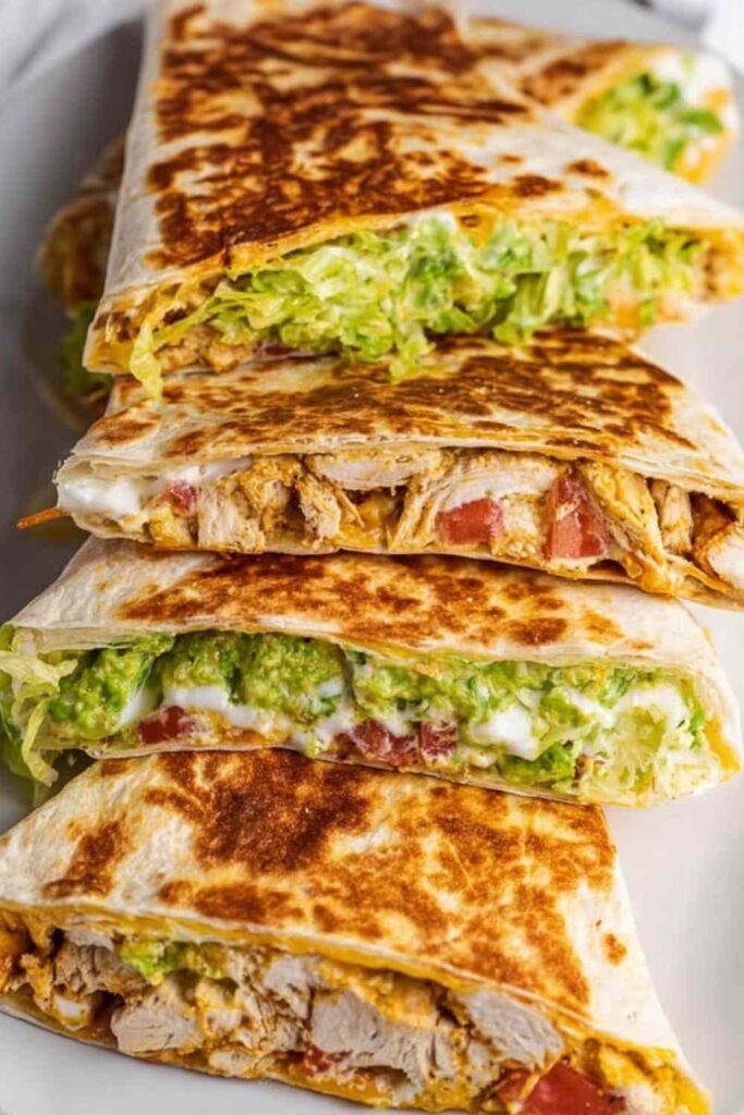 Homemade chicken crunchwrap supreme cut in half diagonally showing crispy tostada shell with layers of shredded chicken, queso blanco, guacamole, and melted Monterey Jack cheese inside a golden flour tortilla