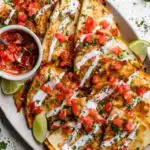 Crispy chicken fajita quesadilla sliced into wedges on a wooden board with salsa and sour cream