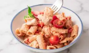 Baked chicken feta pasta in a white baking dish with golden feta, roasted cherry tomatoes, and fresh basil