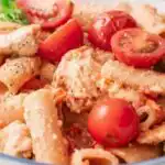 Baked chicken feta pasta in a white baking dish with golden feta, roasted cherry tomatoes, and fresh basil