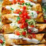 Crispy fried chicken flautas on a plate with sour cream, salsa, and shredded lettuce