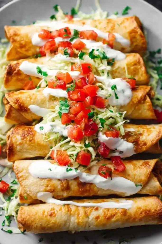 Crispy fried chicken flautas on a plate with sour cream, salsa, and shredded lettuce