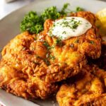 Crispy chicken fried chicken smothered in peppery white gravy on a white plate with mashed potatoes
