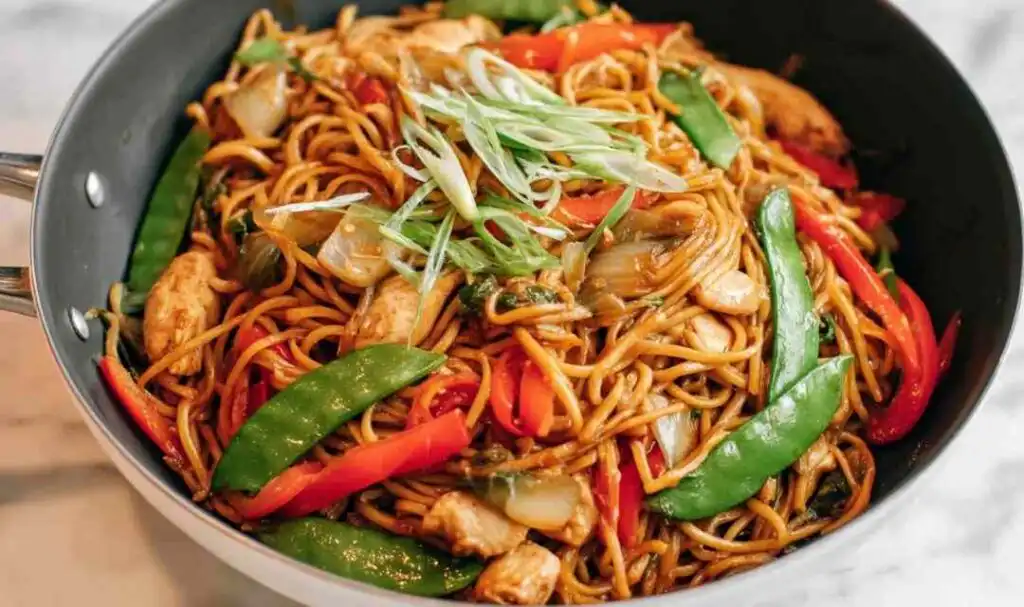 Homemade chicken lo mein with snow peas, carrots, red bell pepper, and mushrooms tossed in a large skillet