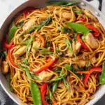 Homemade chicken lo mein with snow peas, carrots, red bell pepper, and mushrooms tossed in a large skillet