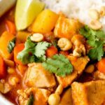Chicken Massaman Curry served over jasmine rice in a bowl, garnished with roasted peanuts, fresh cilantro, and a lime wedge