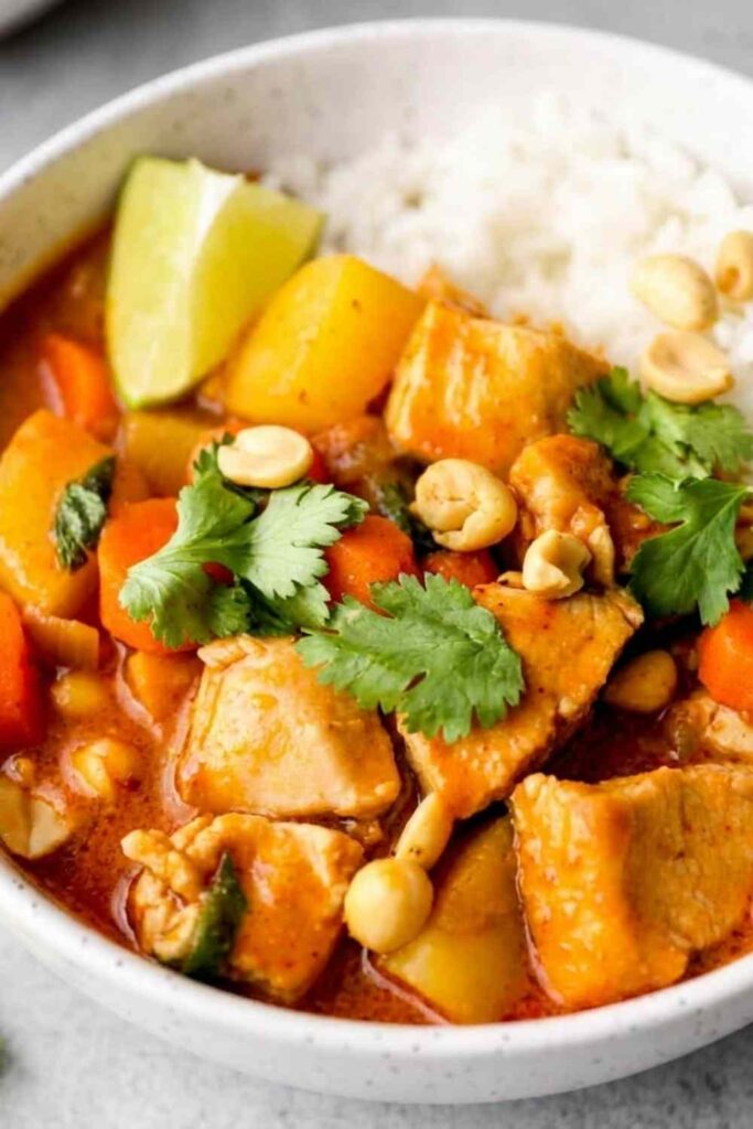 Chicken Massaman Curry served over jasmine rice in a bowl, garnished with roasted peanuts, fresh cilantro, and a lime wedge