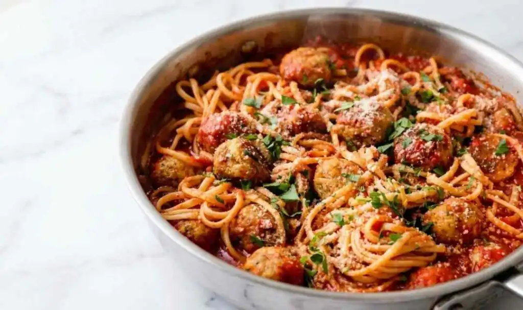 Chicken meatballs and spaghetti in a large pan with homemade tomato sauce topped with Parmesan and fresh parsley