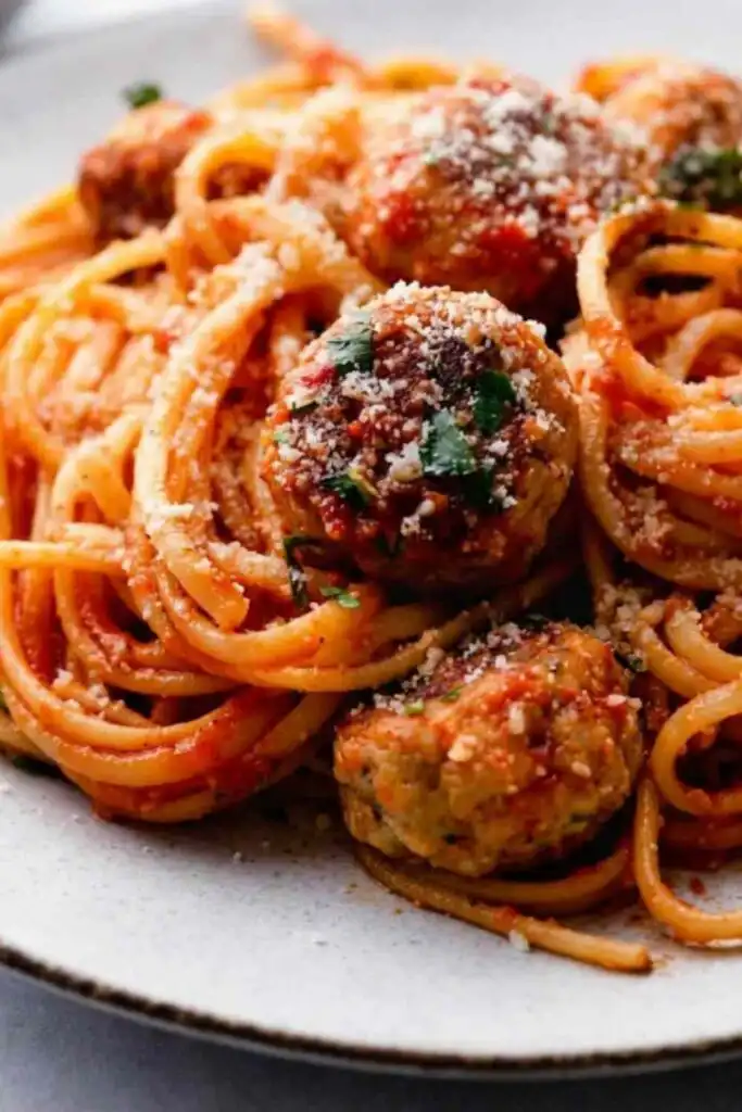 Chicken meatballs and spaghetti in a large pan with homemade tomato sauce topped with Parmesan and fresh parsley