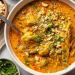 A bowl of chicken mulligatawny soup topped with roasted cashews and fresh cilantro on a rustic wooden table