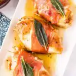 Chicken Saltimbocca with crispy prosciutto and fresh sage in white wine butter sauce on a white dinner plate