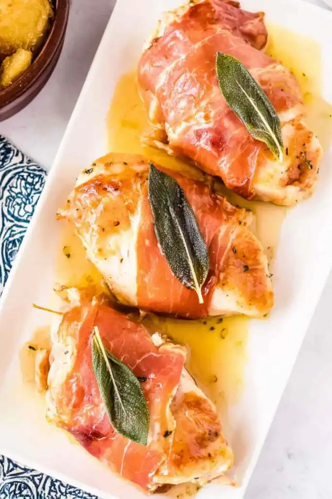 Chicken Saltimbocca with crispy prosciutto and fresh sage in white wine butter sauce on a white dinner plate