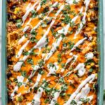 Chicken tamale casserole in a 9x13 baking dish topped with melted cheddar cheese and fresh cilantro