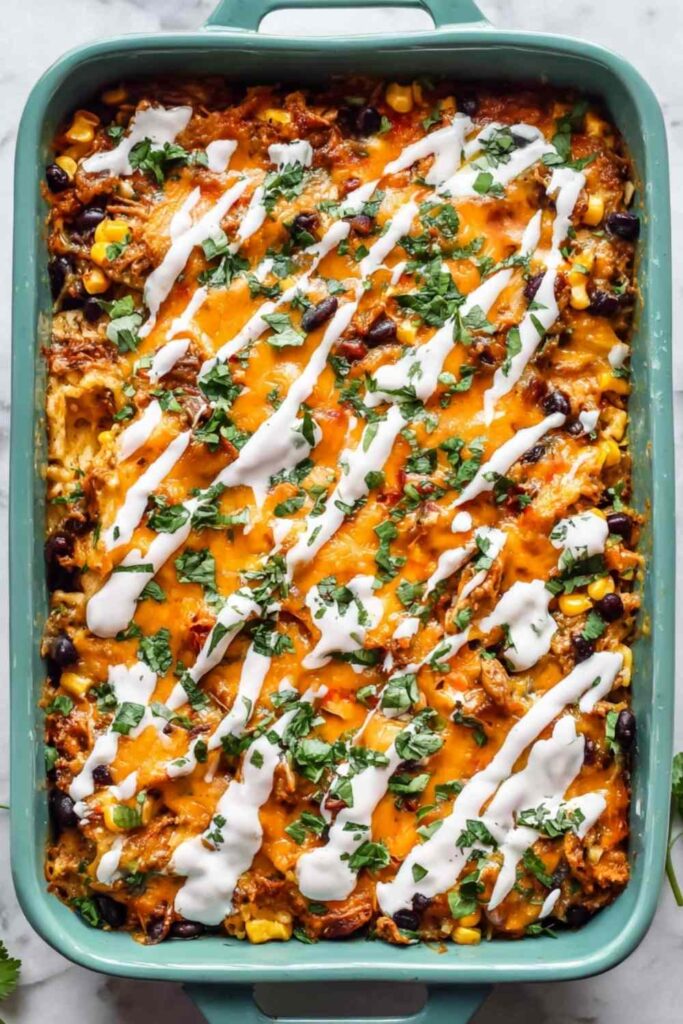Chicken tamale casserole in a 9x13 baking dish topped with melted cheddar cheese and fresh cilantro