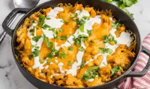 Chicken tamale pie in a cast iron skillet topped with melted Mexican cheese and fresh cilantro
