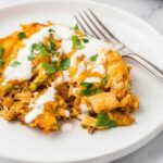 Chicken tamale pie in a cast iron skillet topped with melted Mexican cheese and fresh cilantro