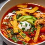 Bowl of homemade chicken tortilla soup topped with crispy baked tortilla strips, shredded cheddar, and fresh cilantro