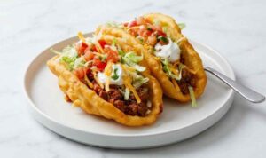 Copycat chalupas with crispy homemade shells filled with seasoned ground beef, sour cream, lettuce, tomatoes, and cheddar cheese on a wooden board