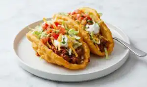Copycat chalupas with crispy homemade shells filled with seasoned ground beef, sour cream, lettuce, tomatoes, and cheddar cheese on a wooden board