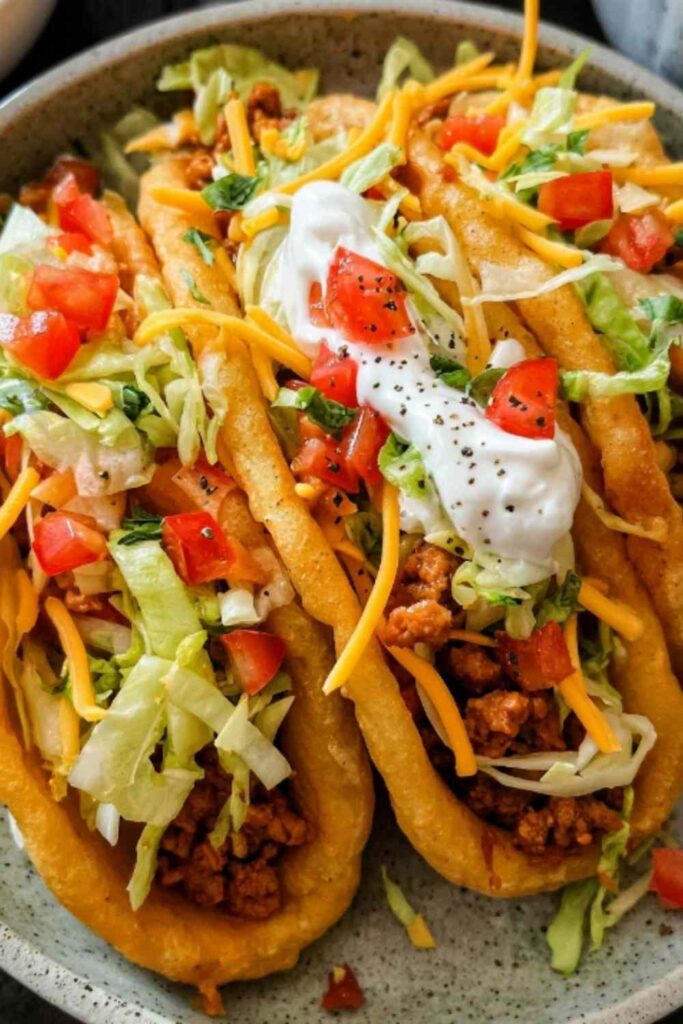 Copycat chalupas with crispy homemade shells filled with seasoned ground beef, sour cream, lettuce, tomatoes, and cheddar cheese on a wooden board