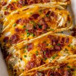 Crack chicken tacos baked in crunchy shells topped with melted cheese and crispy bacon