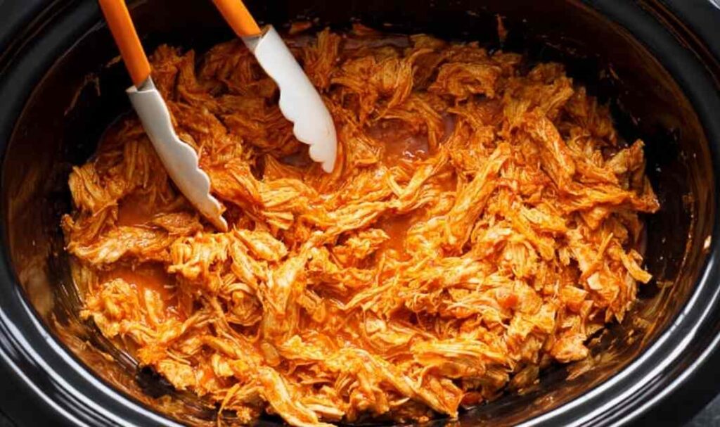 Chicken breasts cooking in buffalo sauce and butter inside a crockpot on high setting