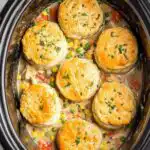 Crockpot chicken pot pie recipe served in a bowl topped with a golden fluffy biscuit brushed with garlic butter