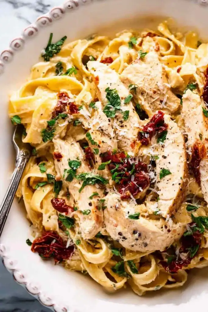 Creamy Crockpot Tuscan chicken served over fettuccine pasta with sun-dried tomatoes and Parmesan