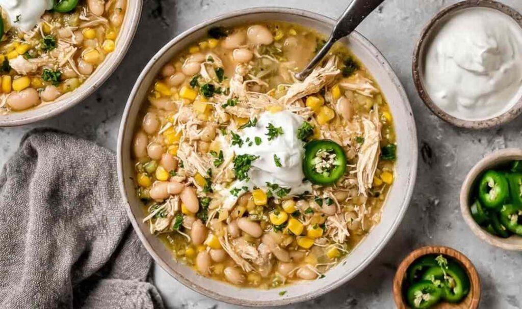 A bowl of creamy Crockpot white chicken chili topped with sliced jalapeno, fresh cilantro, and a dollop of sour cream