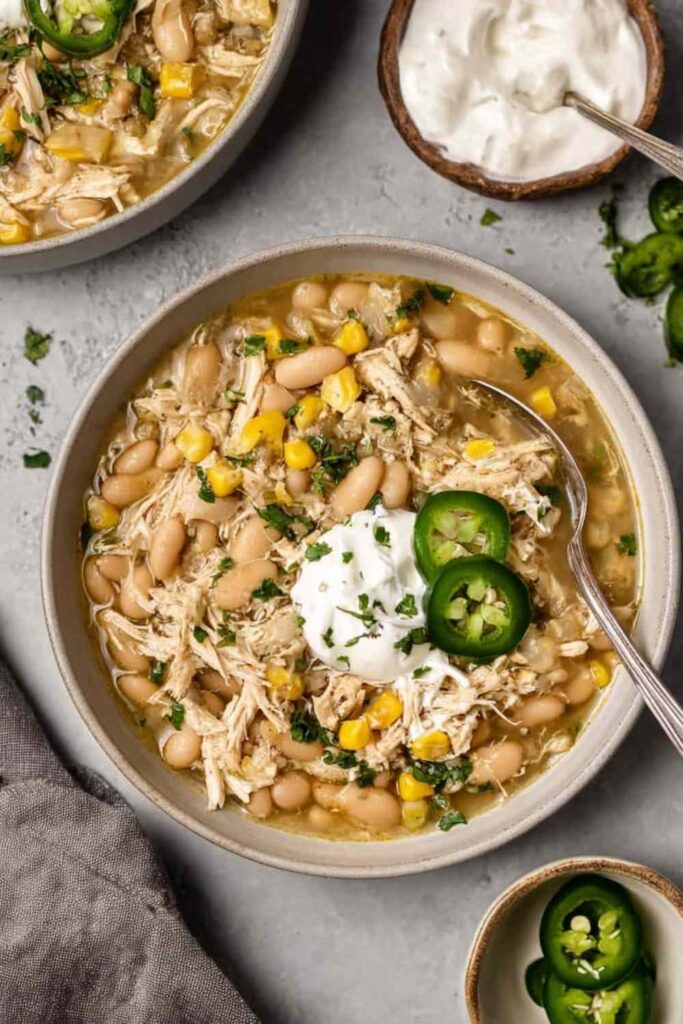 A bowl of creamy Crockpot white chicken chili topped with sliced jalapeno, fresh cilantro, and a dollop of sour cream
