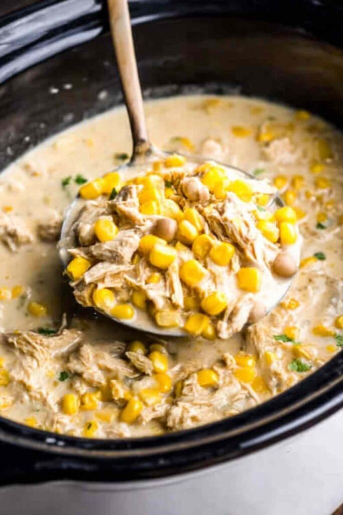 Crockpot white chicken enchilada soup recipe served in a bowl topped with avocado, sour cream, shredded cheese, and tortilla strips