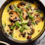 A bowl of homemade egg drop soup with silky egg ribbons, sliced cremini mushrooms, and chopped green onions in a golden chicken broth