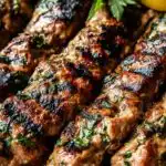 Grilled chicken kafta skewers on a plate with warm pita bread and lemon wedges