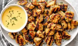 Grilled chicken nuggets with golden grill marks on a white plate with honey mustard dipping sauce