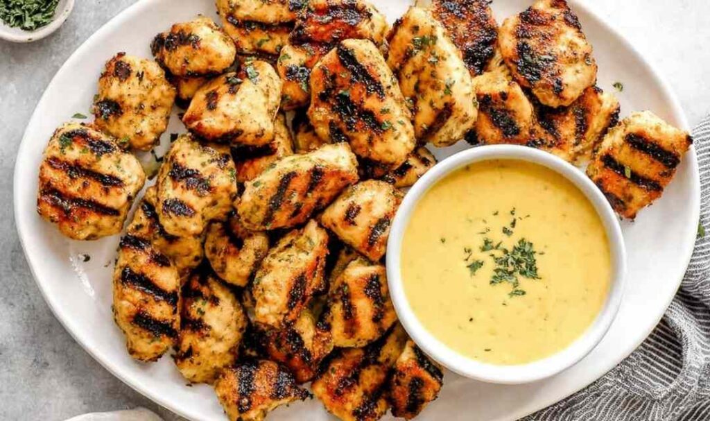 Grilled chicken nuggets with golden grill marks on a white plate with honey mustard dipping sauce