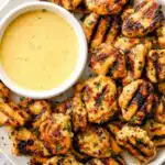 Grilled chicken nuggets with golden grill marks on a white plate with honey mustard dipping sauce