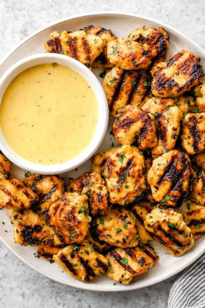 Grilled chicken nuggets with golden grill marks on a white plate with honey mustard dipping sauce