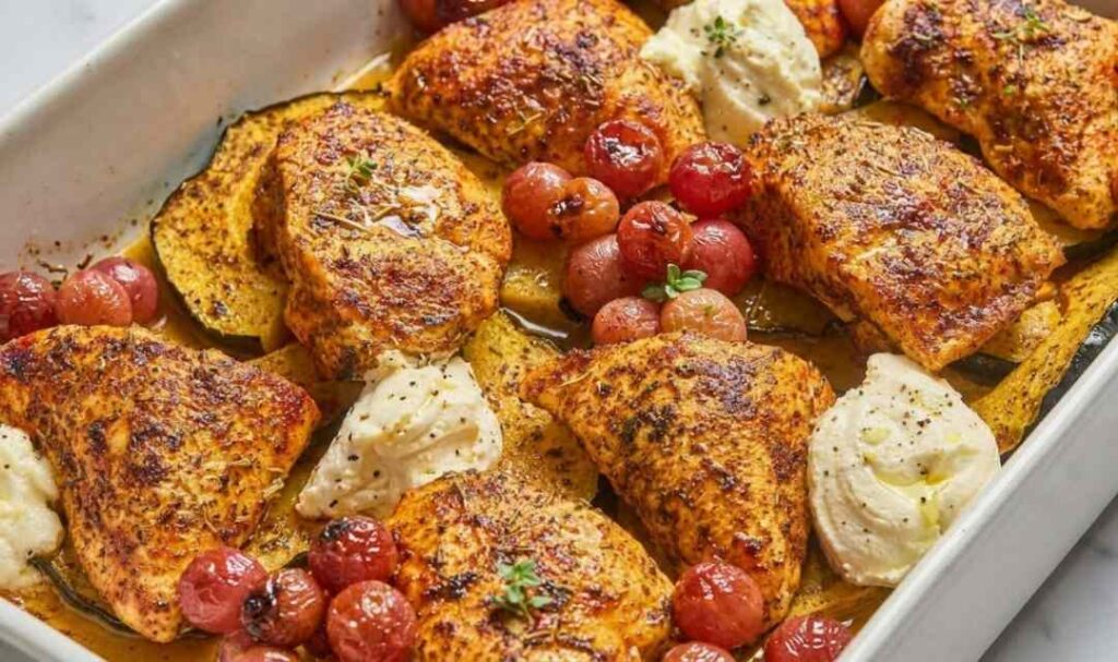 Herb roasted chicken with grapes acorn squash and ricotta served in a white ceramic baking dish with creamy ricotta dollops on top
