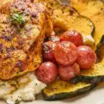 Herb roasted chicken with grapes acorn squash and ricotta served in a white ceramic baking dish with creamy ricotta dollops on top