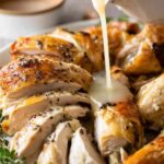 Homemade chicken gravy poured over creamy mashed potatoes in a white bowl
