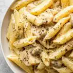 Instant Pot cheesy chicken pasta served in a white bowl topped with freshly grated cheddar and parsley